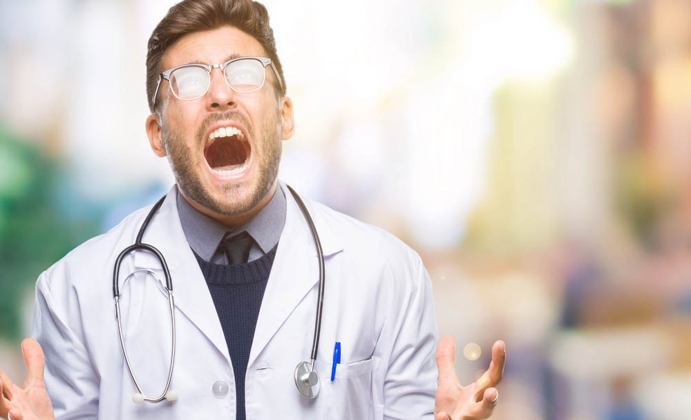 A male doctor appears to scream in frustration. His glasses catch the light 