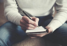 The Wound That Speaks A man is sitting on a sofa and writing notes in a notebook