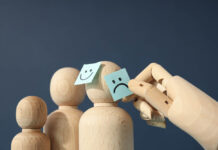 Family Traditions and the Inheritance of “Madness” A wooden hand touches post it notes of smiling and sad faces on wooden figures