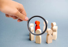 Madness Is a Human Phenomenon Magnifying glass is looking at the People stand in a circle on a gray background. Communication. Business team, teamwork, team spirit. Wooden figures of people. A circle of people. Selective focus
