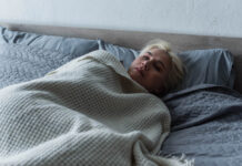 Inertia as Neuroceptive State Beyond the Pathologizing Lens A young blonde woman looks sad in bed with the covers up to her neck