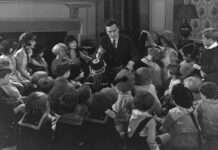 Narrative Reclamation: Who’s Allowed to Tell Their Story? BW photo. Man in a suit telling children