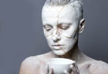 It’s the Cracked Ones Who Let the Light in Close-up of a person covered in white paint with gold cracks, kintsugi style
