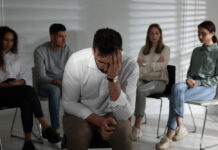 Reflections on My Mistrust for Other Mental Health Workers Unhappy man and group of people behind his back indoors. Therapy session