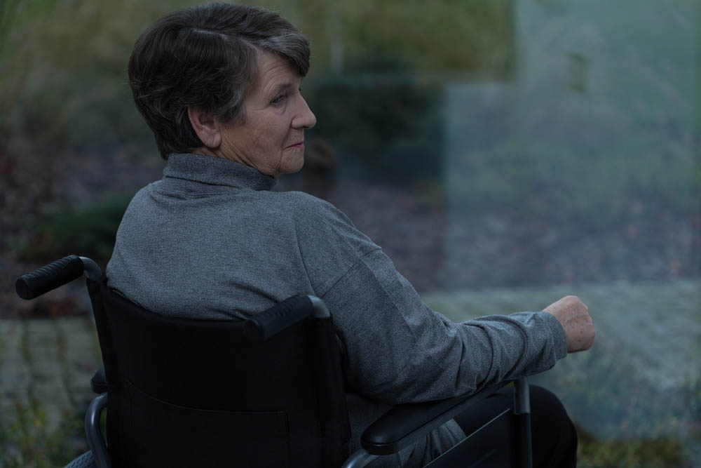 Elderly sad woman looking through the window