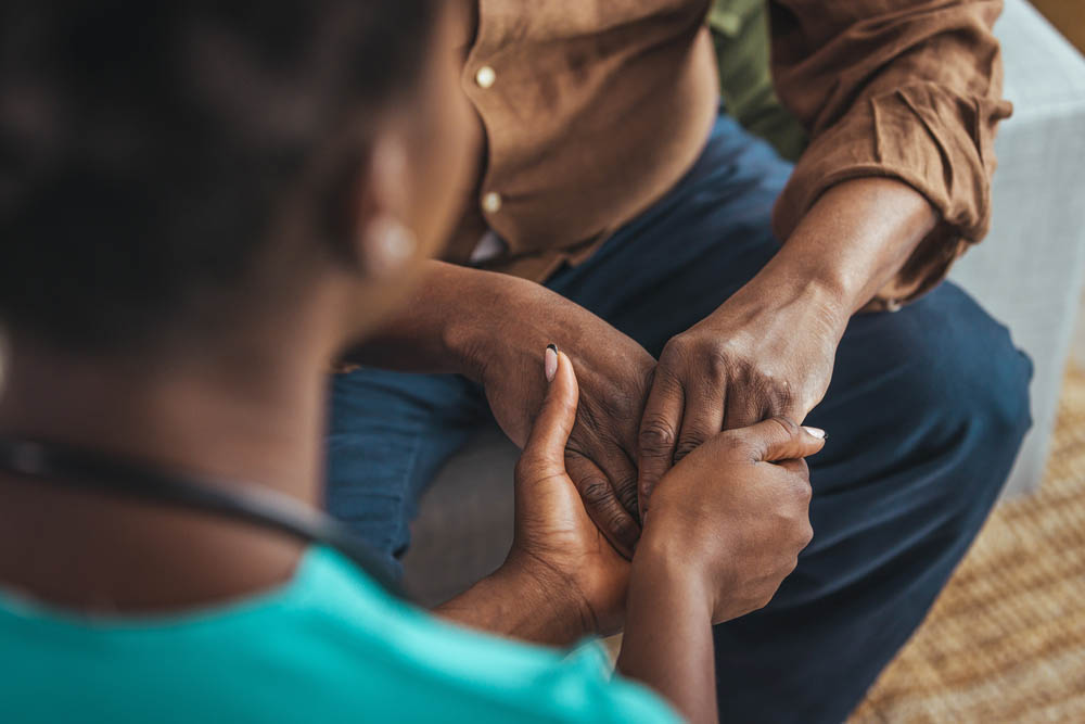 Female healthcare worker holding hands of senior man at care home, focus on hands. Doctor helping old patient with Alzheimer's disease. Female carer holding hands of senior man
