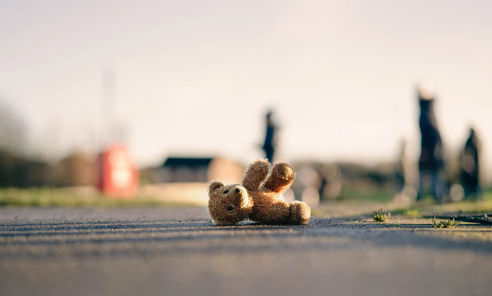 Lost teddy bear lying on the road with blurry people in the background