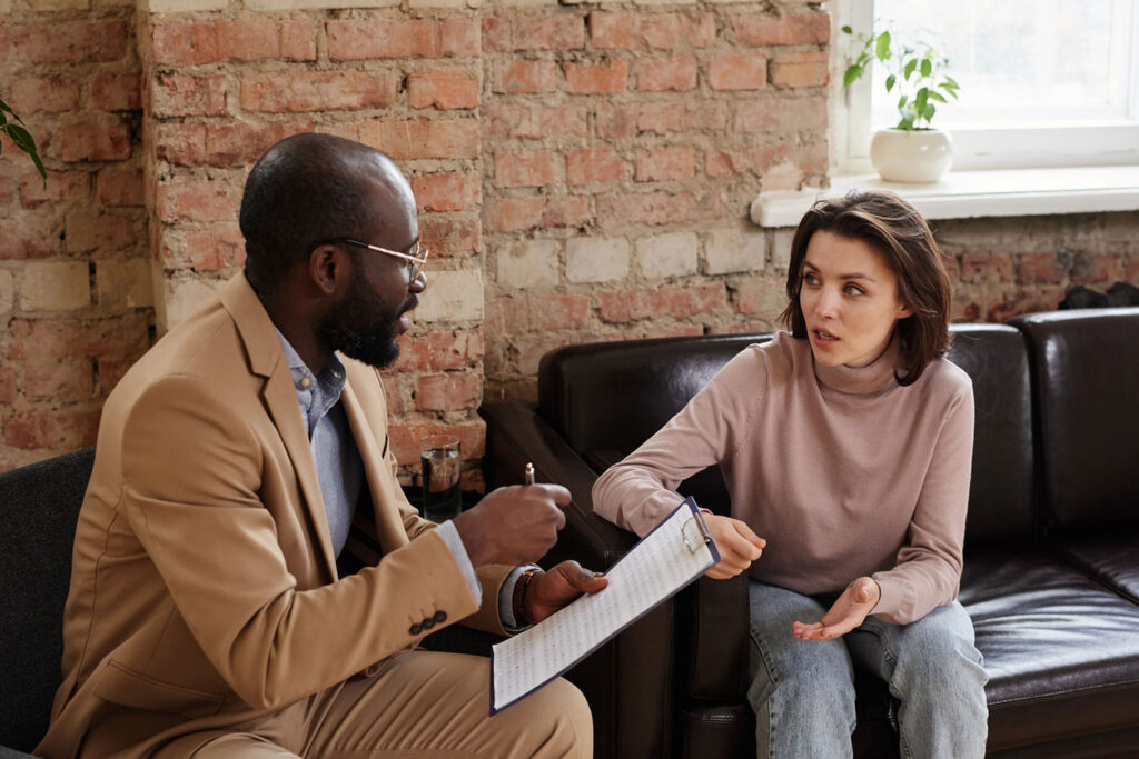 African-American psychologist in eyeglasses sitting with clipboard and working with problems of patient in loft office