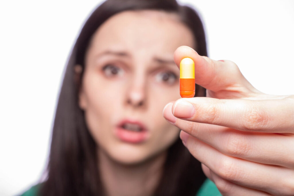 Woman out of focus holding pill toward camera