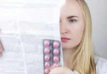 A blonde white woman reads the product label for drugs in blister pack in her hand